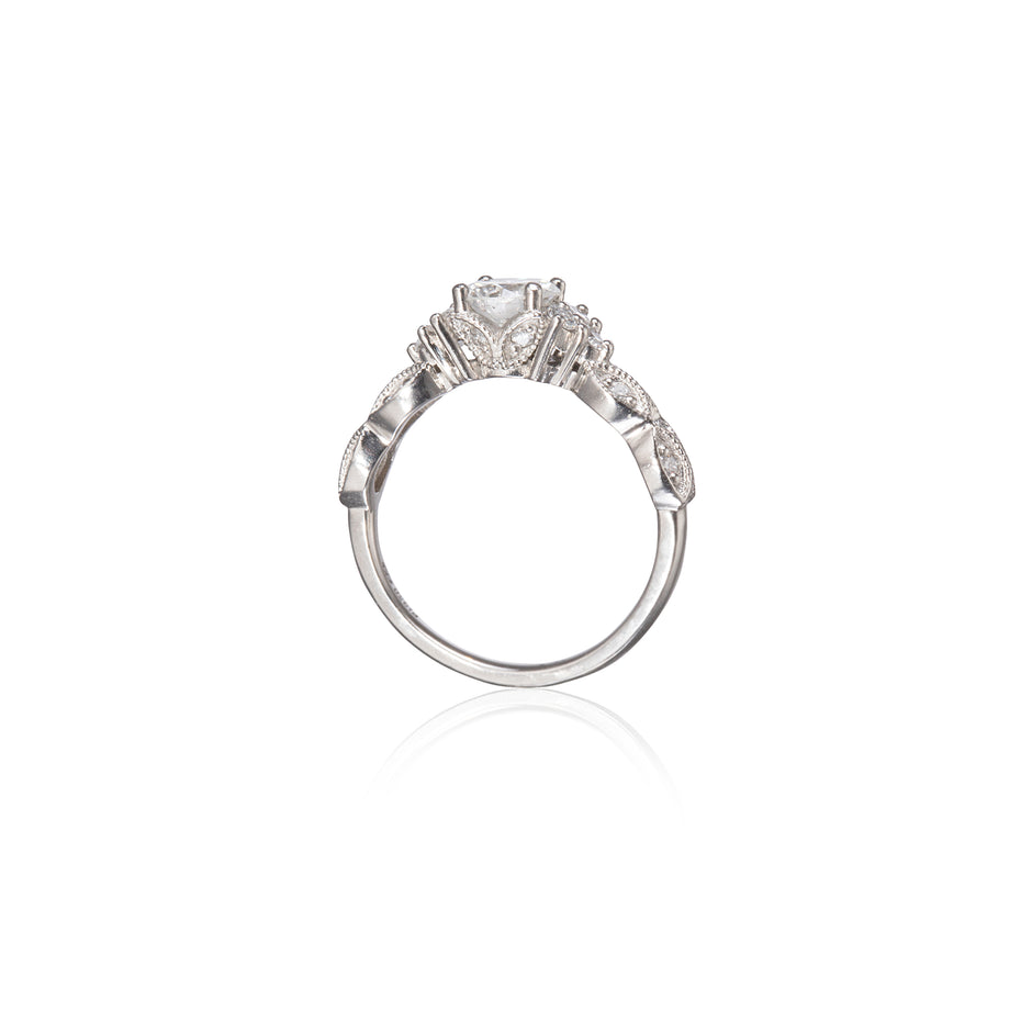A platinum diamond ring with a central round-cut diamond and smaller diamonds along the shoulders, shown on a clean white background with a soft reflection below.