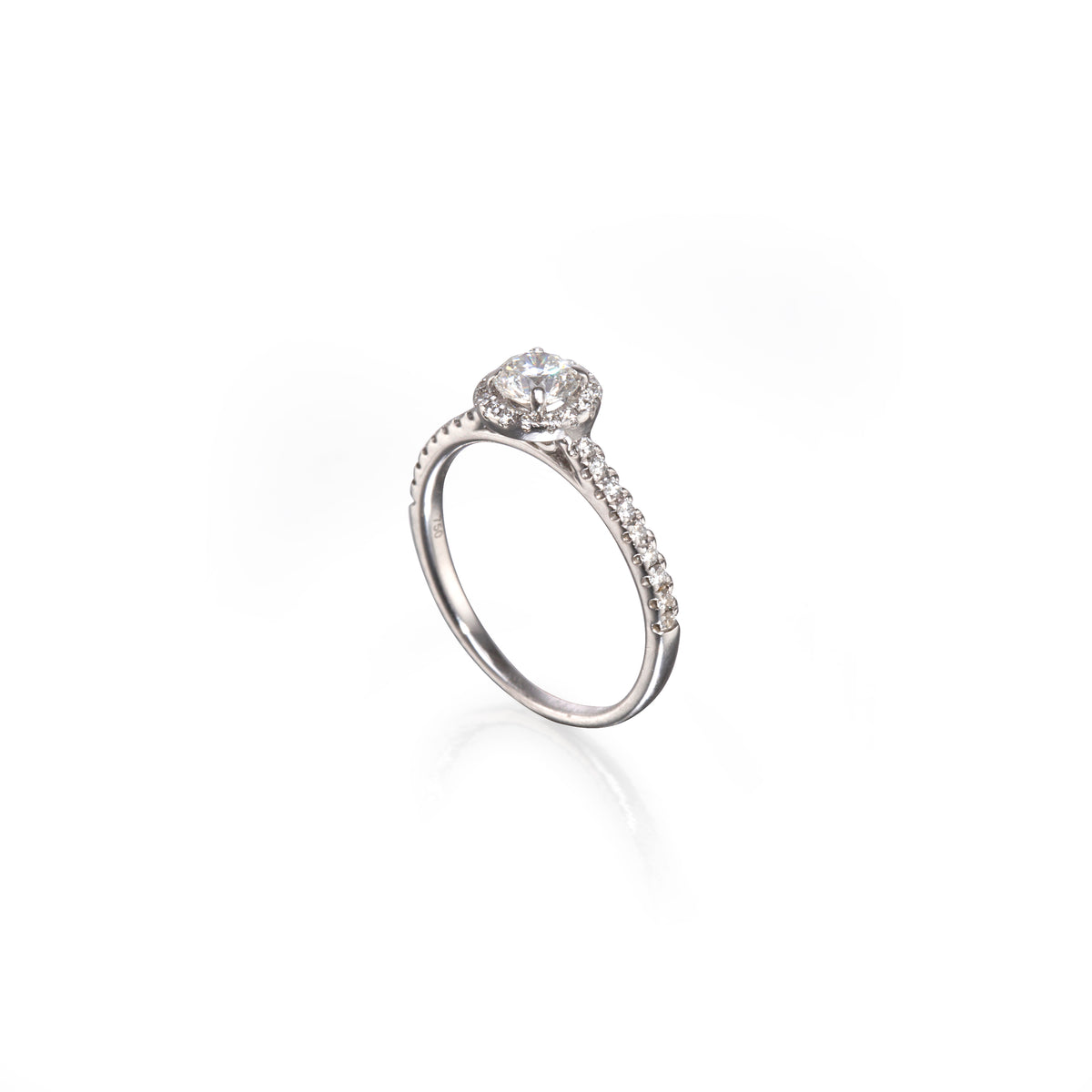 A white gold diamond engagement ring with a round-cut center stone and a pavé-set band, shown on a clean white background with a soft reflection.