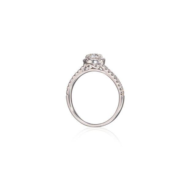 A white gold diamond ring with a round-cut center stone and a pavé band, shown on a clean white background with a soft reflection below.