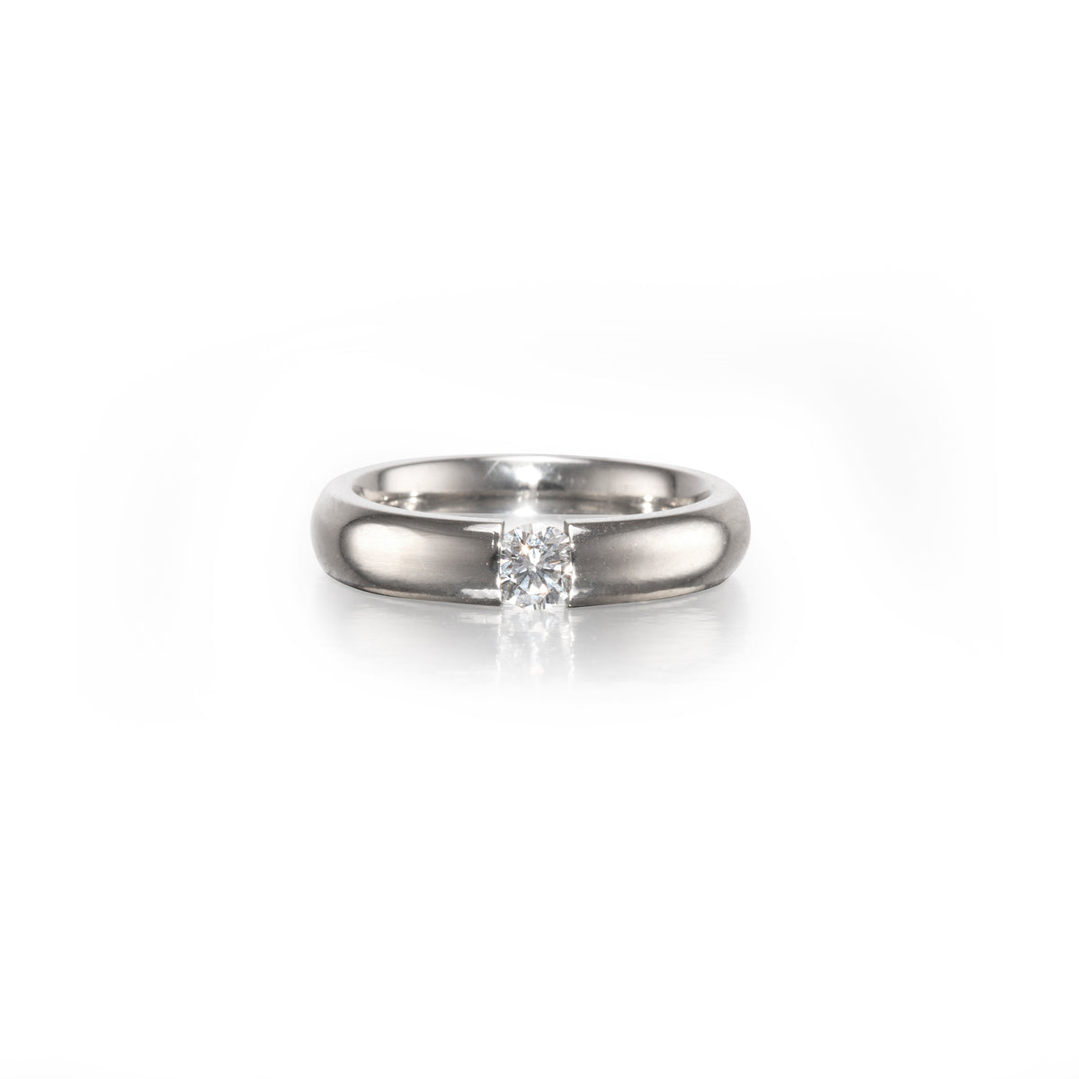A classic solitaire engagement ring featuring a round brilliant-cut diamond set in a polished platinum band, centered on a clean white background with a soft reflection.