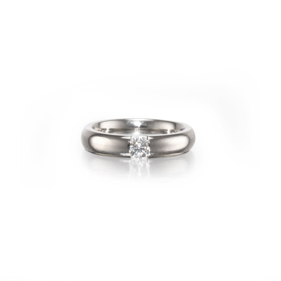 A classic solitaire engagement ring featuring a round brilliant-cut diamond set in a polished platinum band, centered on a clean white background with a soft reflection.