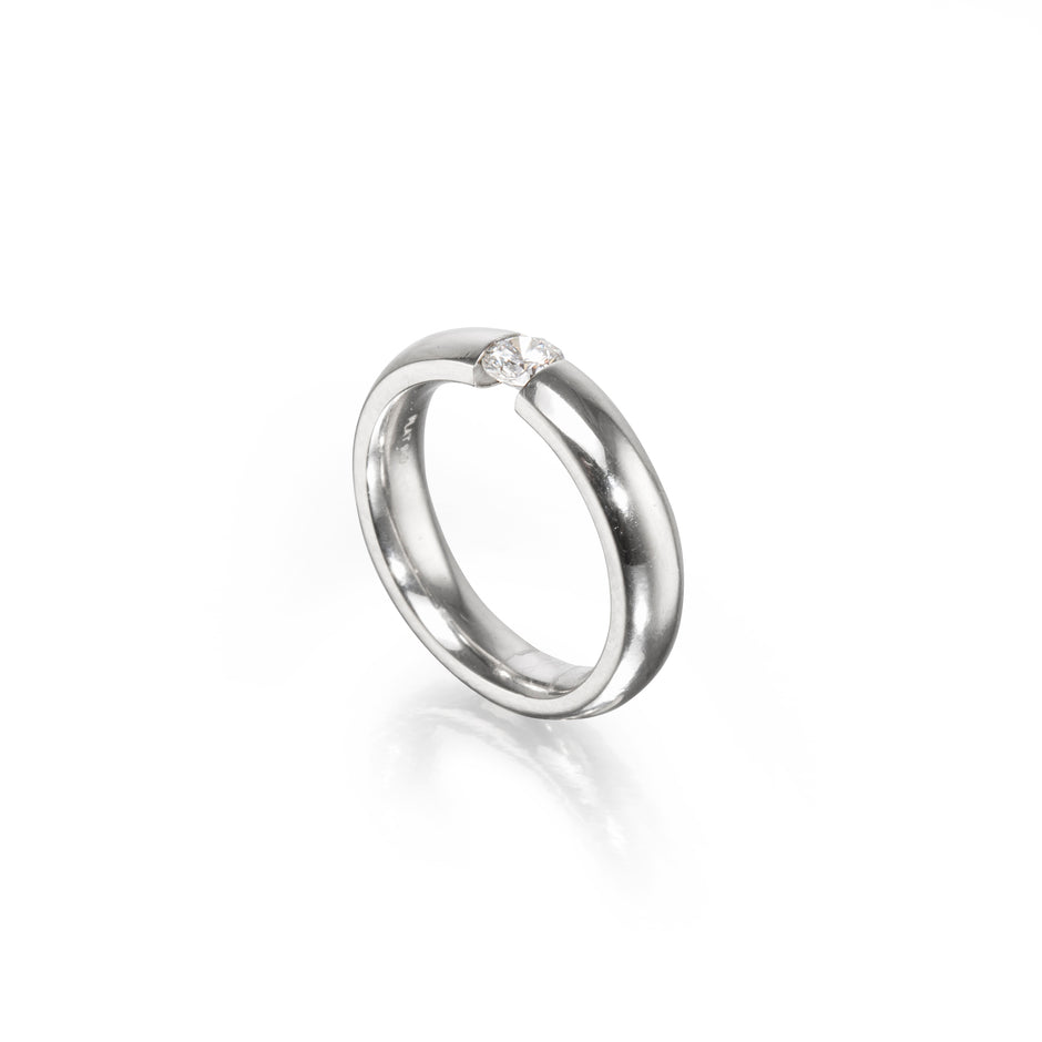 A polished platinum band ring with a single small clear gemstone set near the top, photographed on a clean white background with a soft reflection below