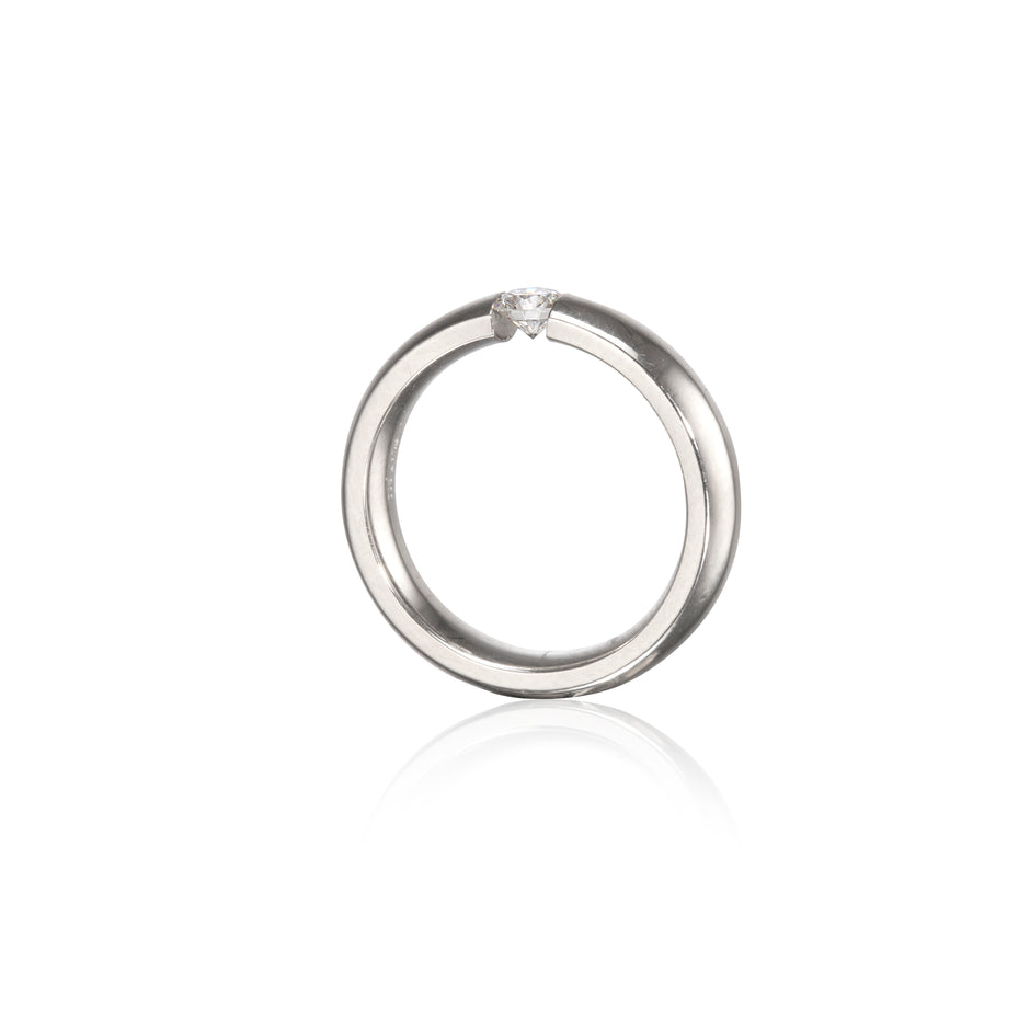 A polished platinum circular ring with a single small clear gemstone set at the top, shown on a clean white background with a soft reflection below.
