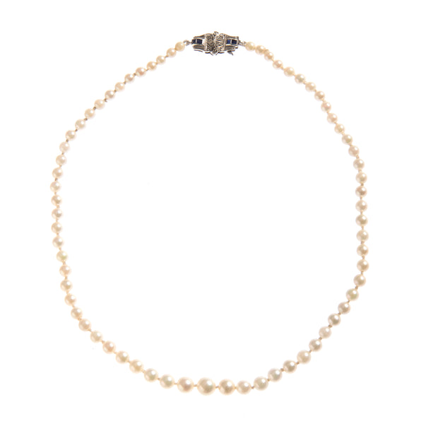 A classic pearl necklace with a white gold clasp featuring small dark blue inlays, displayed on a clean white background.