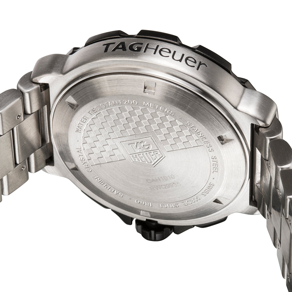 Close-up of the back of a TAG Heuer watch showing the brushed stainless steel case back with engraved details and the brand name 'TAG Heuer' on the crown guard.