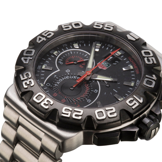 A close-up shot of a men's analog watch TAG, featuring a black dial with silver-tone hands, a red second hand, and a black bezel with white numerals, paired with a stainless steel link bracelet.