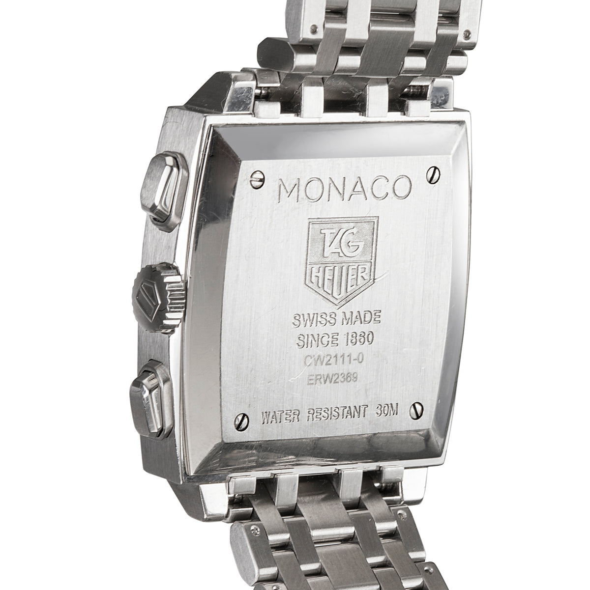 Close-up of the back of a stainless steel watch case with a metal link bracelet, showing engraved text reading MONACO and the TAG Heuer logo on a white background.