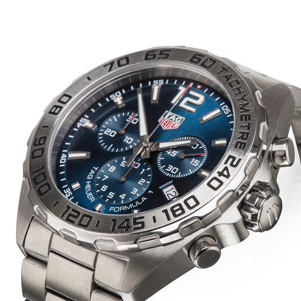 A Tag Heuer Formula 1 wristwatch with a silver stainless steel case and bracelet, featuring a blue dial with three sub-dials and a black tachymeter bezel.
