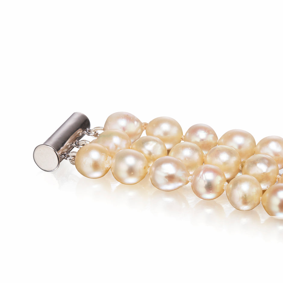 A close-up of a pearl strand bracelet with a silver-toned toggle clasp, showing lustrous cream to pale gold pearls on a white background.