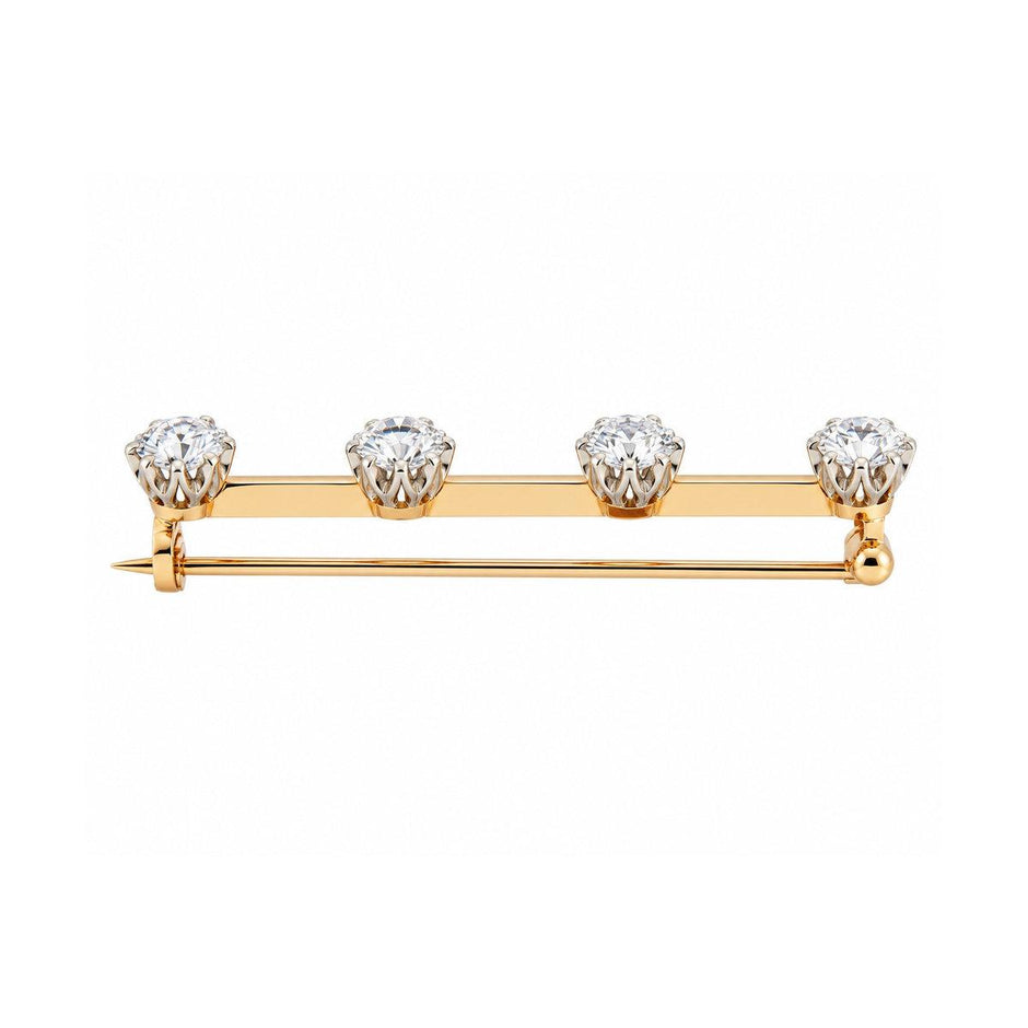 A yellow and rose gold bar pin featuring four round-cut clear gemstones set in a row, photographed on a solid white background.
