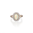 An oval halo ring featuring a central iridescent white opal surrounded by a halo of small clear stones, set in a rose gold band, on a clean white background with a soft reflection.