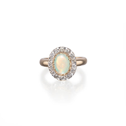 An oval halo ring featuring a central iridescent white opal surrounded by a halo of small clear stones, set in a rose gold band, on a clean white background with a soft reflection.