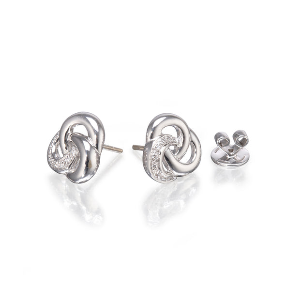 A pair of white gold knot stud earrings with a curved clear crystal accent, shown alongside a matching back clip on a reflective white surface.