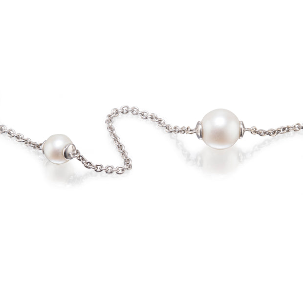 A white gold chain necklace featuring two white freshwater pearls, one larger pearl on the right and one smaller pearl on the left, both set in silver bezels, displayed on a clean white background with soft reflections.